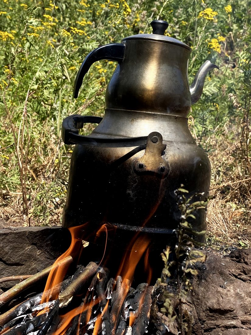 A blackened çaydanlık teapot brewing over an open wood fire