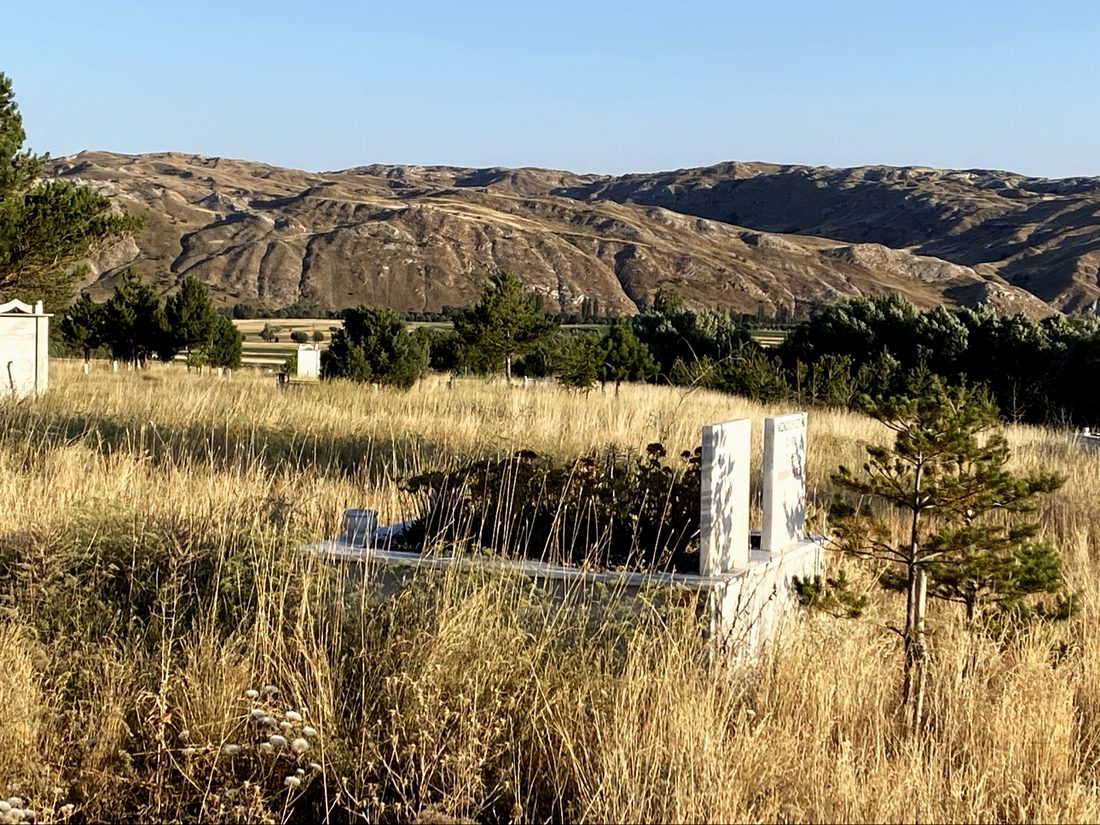 A grave in dry grass beneath bare Anatolian hills