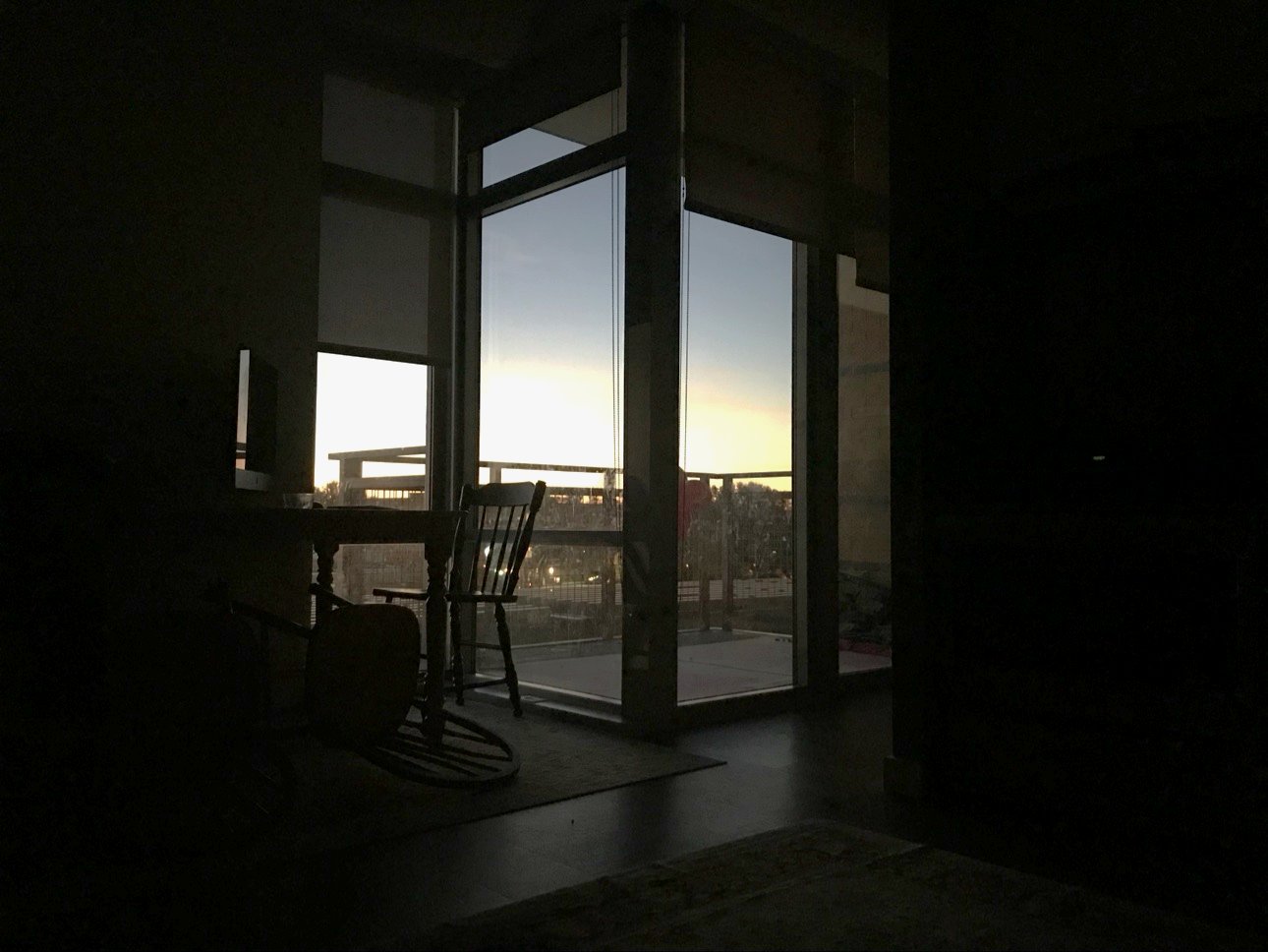 Two chairs in a dark room, facing tall windows at first light