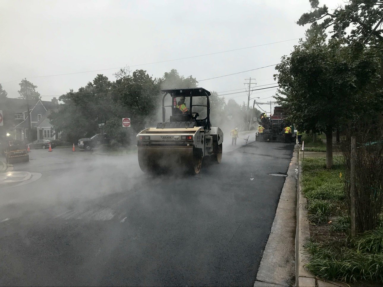 A road roller steaming in the rain on fresh asphalt