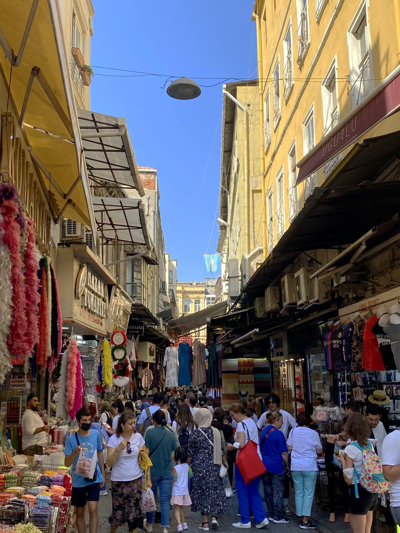 A crowded bazaar street, stalls and shoppers under a hard blue sky
