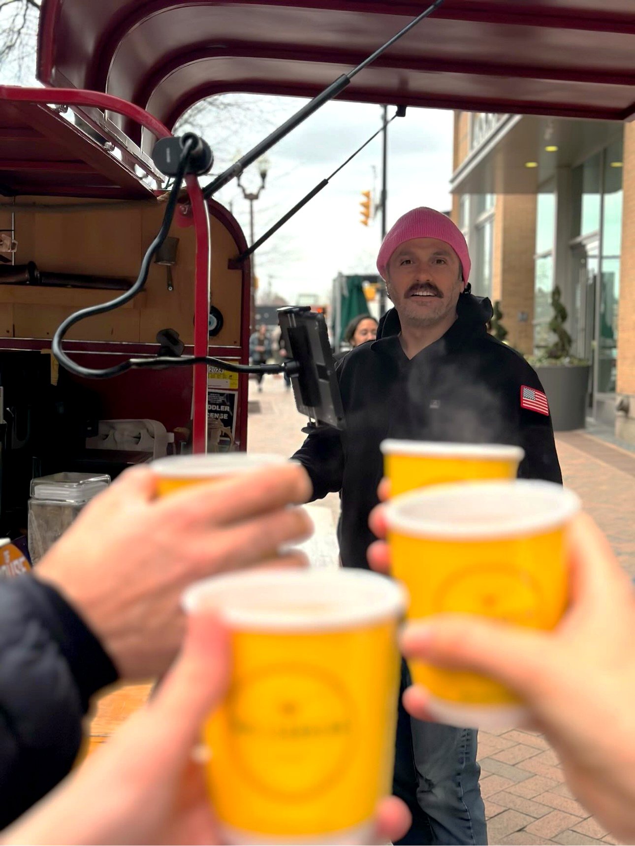 Isa behind his coffee cart, customers raising yellow cups